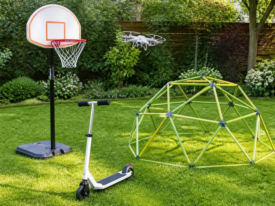 Kids outdoor toys: basketball hoop, drone, scooter and climbing dome on a lawn